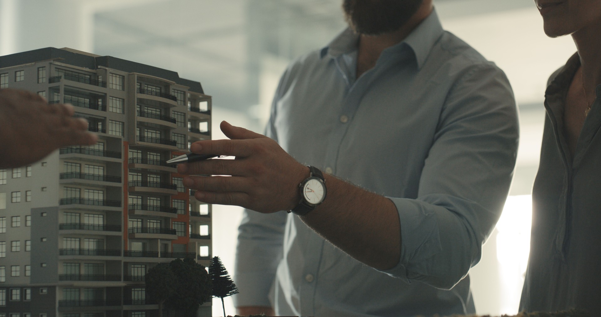 Architects using model apartment block or office to discuss building. Diverse group of engineer colleagues using minature 3D design of blueprints. Contractors thinking, talking, planning development